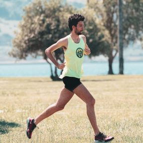 Side view of young determined male athlete in sportswear running on lawn in park near lake in sunny morning